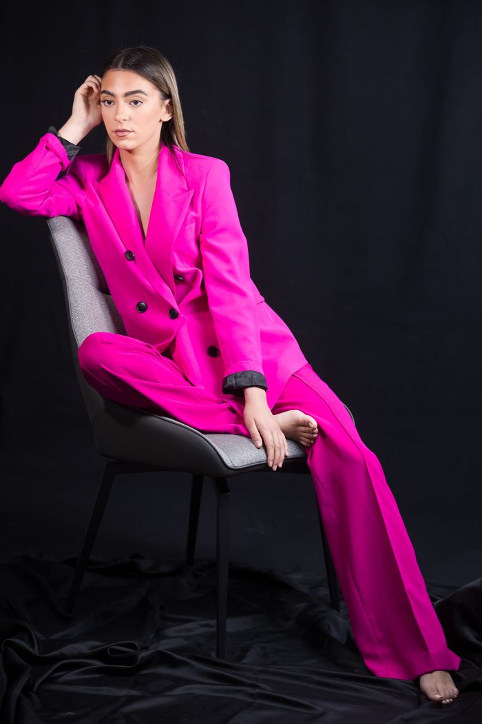 Jeune fille brune aux yeux noirs, vêtue d'un ensemble fuchsia avec blazer et pantalon, posant avec une attitude sereine sous une lumière de studio