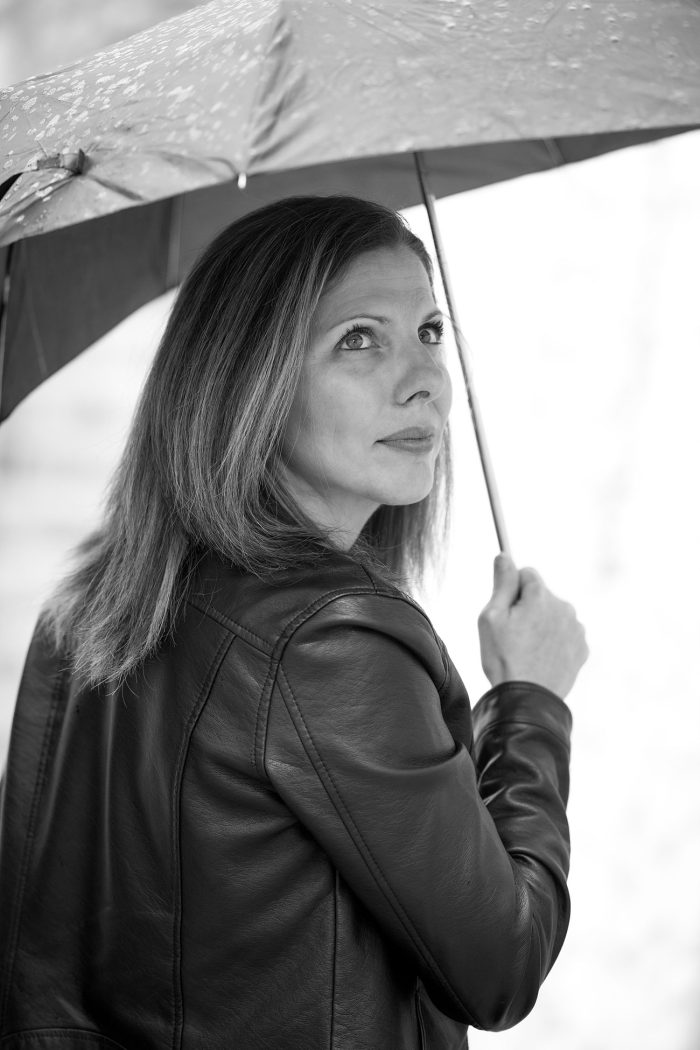 Femme de 40 ans sous la pluie avec un parapluie, pleine d'émotions dans le regard, photo en noir et blanc.